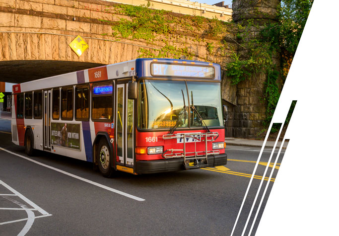 A red, white and blue bus travels under an overpass.